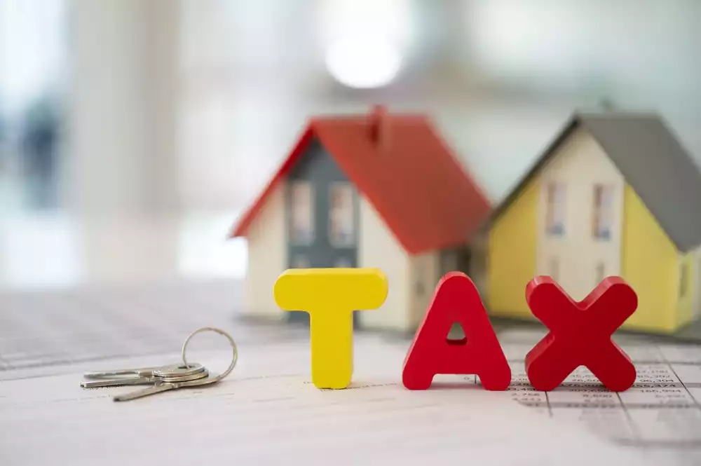 “Tax” spelled out in colorful wooden blocks next to models of homes and a set of keys