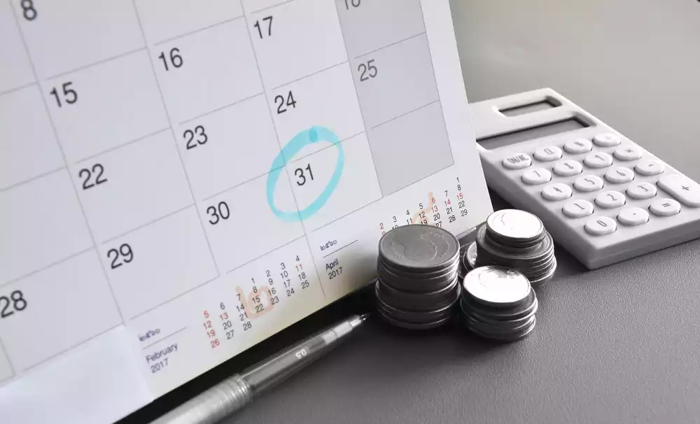 Calendar with the 31 circled in blue next to a stack of change and a calculator representing the idea of property tax payment plans