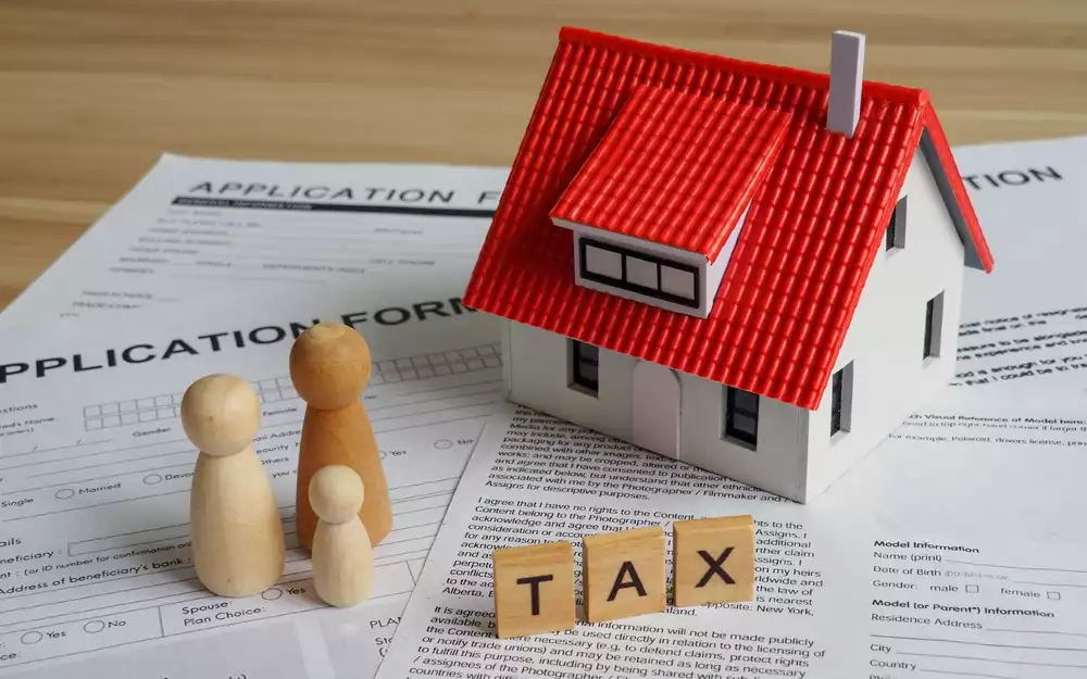 “Tax” written on blocks situated next to a model of a home and application forms
