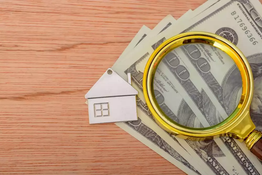 Paper money set against a wooden background with a small keychain of a home representing the idea of hidden costs of unpaid property taxes in TX